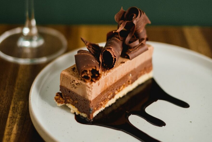 A slice of chocolate torte on a white plate, drizzled with chocolate sauce.