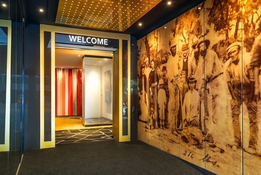 A large mural with an early photo of gold diggers covering a wall at the entrance of Welcome Stranger, with WELCOME written above the door. 