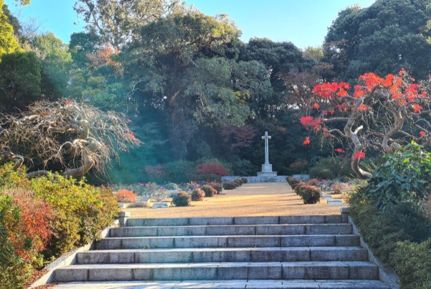 Steps in a landscaped garden leading to a memorial cross, at the Yokohama Commonwealth War Cemetery in Japan.