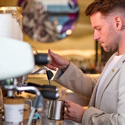 A barista steaming milk at a coffee machine in a cafe.