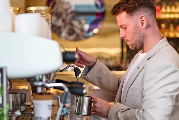 A barista steaming milk at a coffee machine in a cafe.