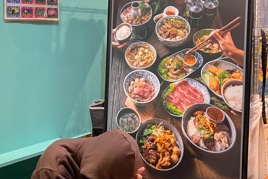 Customer choosing from large menu screen with images of food dishes in a Thai cafe.