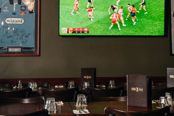 A room inside the Turf Sports Bar with a TV on a wall screening an AFL football match.