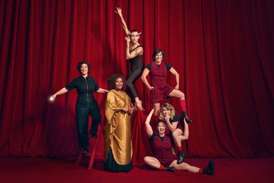 Six performers posing dramatically against a vibrant red stage curtain backdrop.