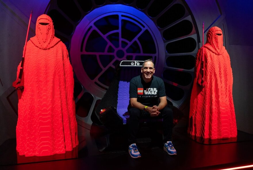 Two figures from Star Wars made from red lego bricks, with a man seated between them.