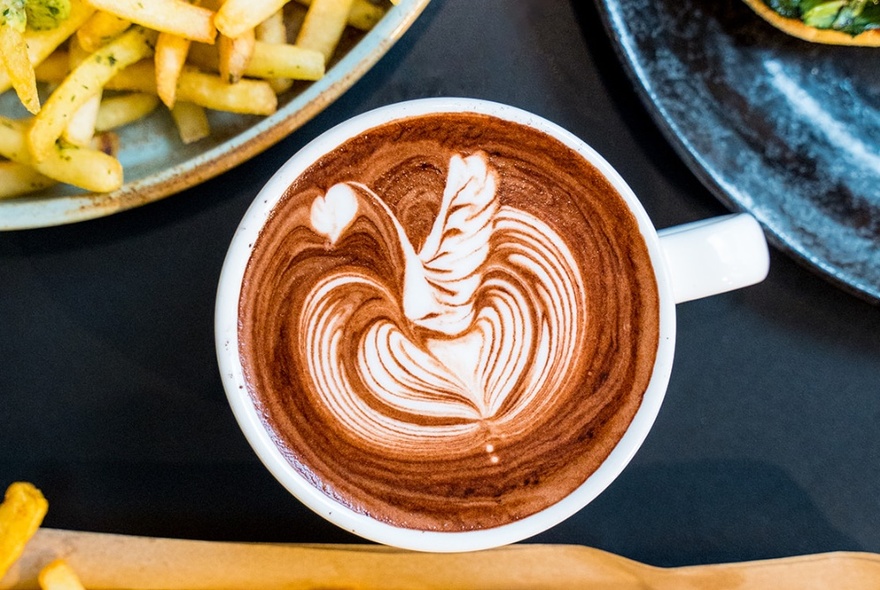 A cup of coffee with swan latte art next to a bowl of chips.