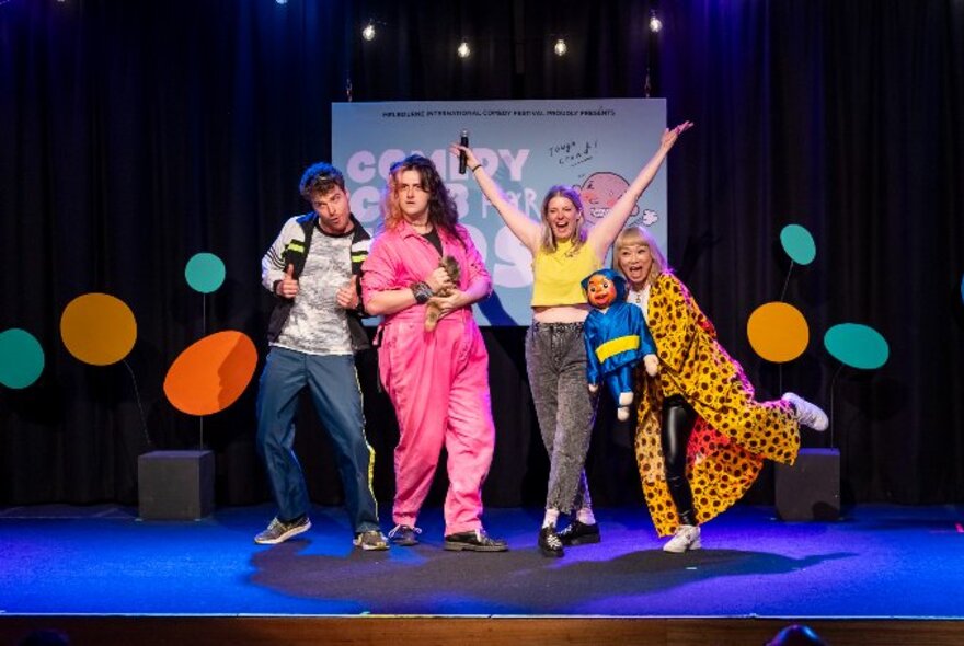 A group of kids' show performers on stage with coloured circles, playing around. 