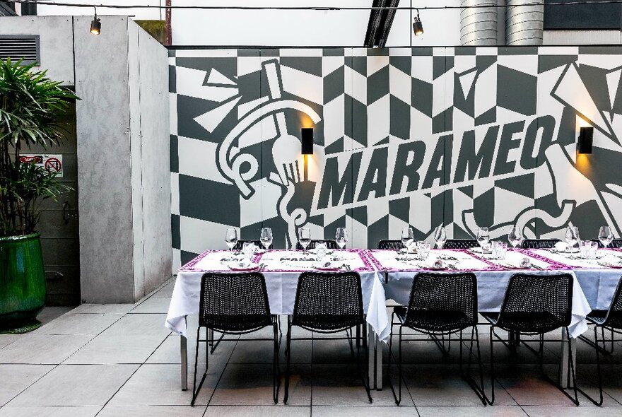 The outdoor courtyard seating area at Marameo restaurant with a black and white painted graphic and the words 'MARAMEO' on the wall.