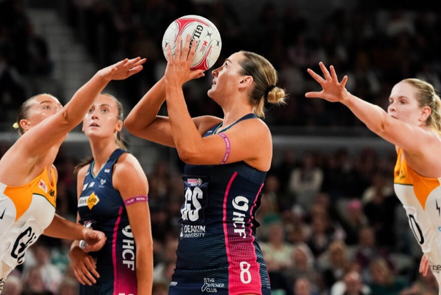 Netball players competing in a game, with one player holding the ball and two players from the opposing team reaching towards her.