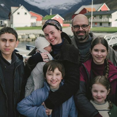 A still image from a film showing a family gathered together for a group shot with a village in the background. 