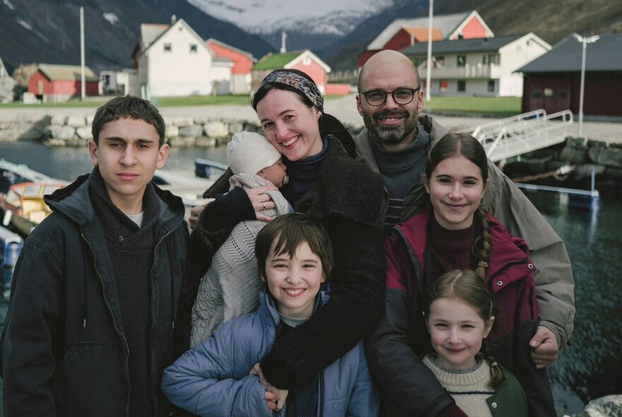 A still image from a film showing a family gathered together for a group shot with a village in the background. 