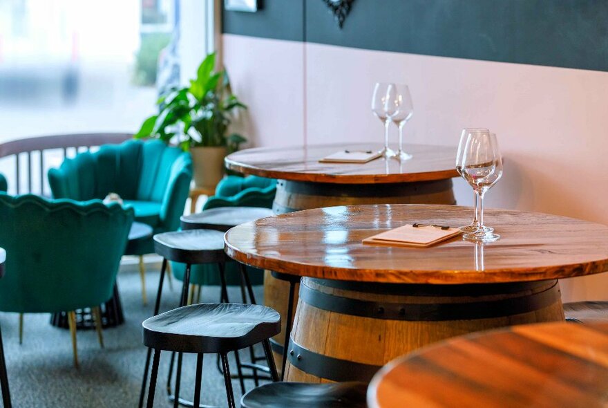 Bar interior with round tables on wine barrels with stools and blue armchairs.