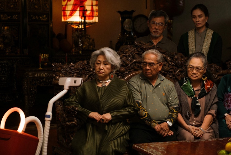 A still image from the film A Useful Ghost wuth people sitting starting at the head of a vacuum cleaner. 