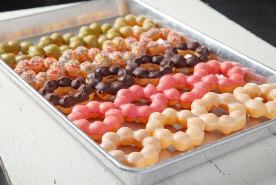 A tray of mochi doughnuts with different coloured icing on each row.