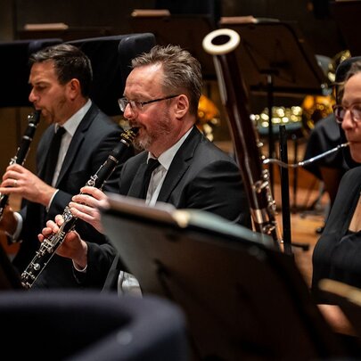 Oboe and clarinet players performing in an orchestra on stage. 