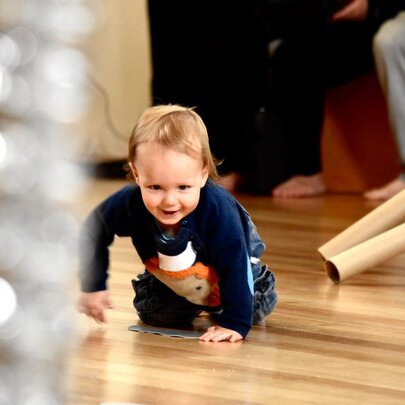 A toddler crawling on a polished wooden floor at an ArtPlay activity.