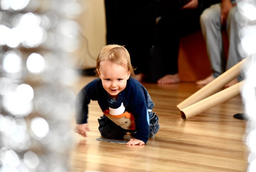 A toddler crawling on a polished wooden floor at an ArtPlay activity.