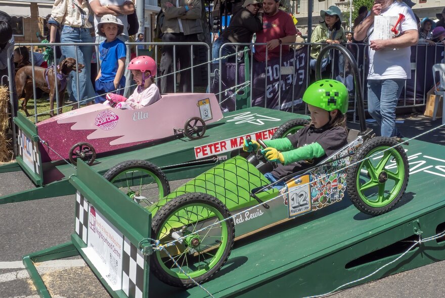 Two billycarts and their drivers on the green starting blocks of a billycart race.