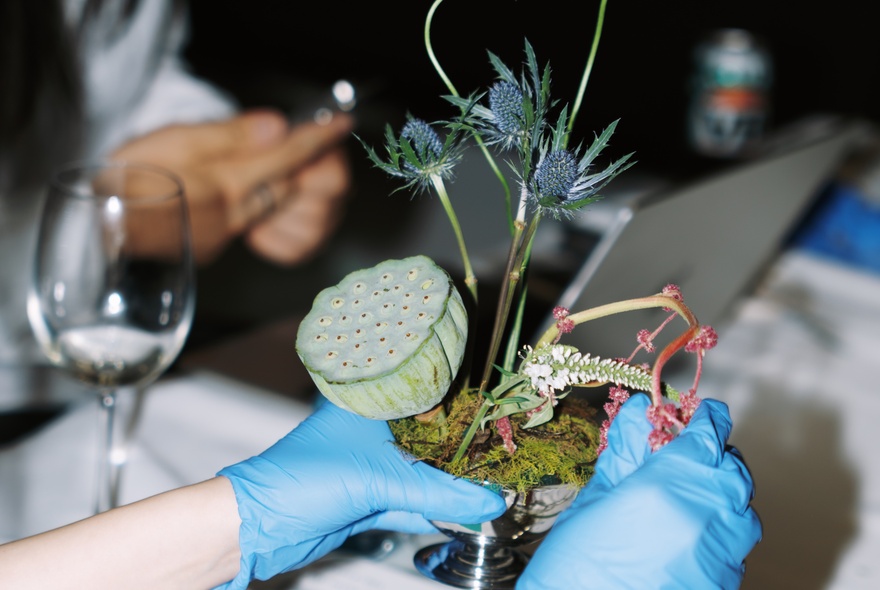 A person wearing blue rubber gloves creating an Ikebana arrangement, which is the traditional Japanese art of flower arranging.