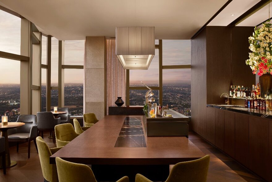 A bar with warm wood interior high up with a view out over the city.