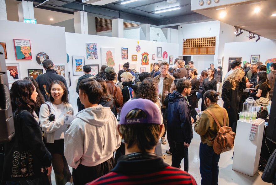 Installation view of an exhibition in a gallery space, with crowds of people in the space mingling and socialising and looking at the art.