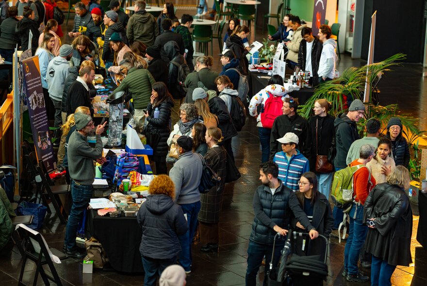 Crowd browsing market stalls in an indoor venue.