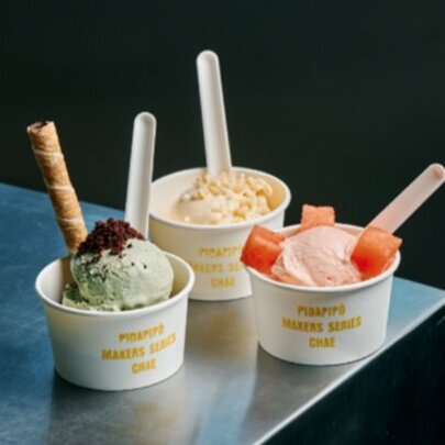 Three cups of ice cream with spoons, fruit and a wafer.