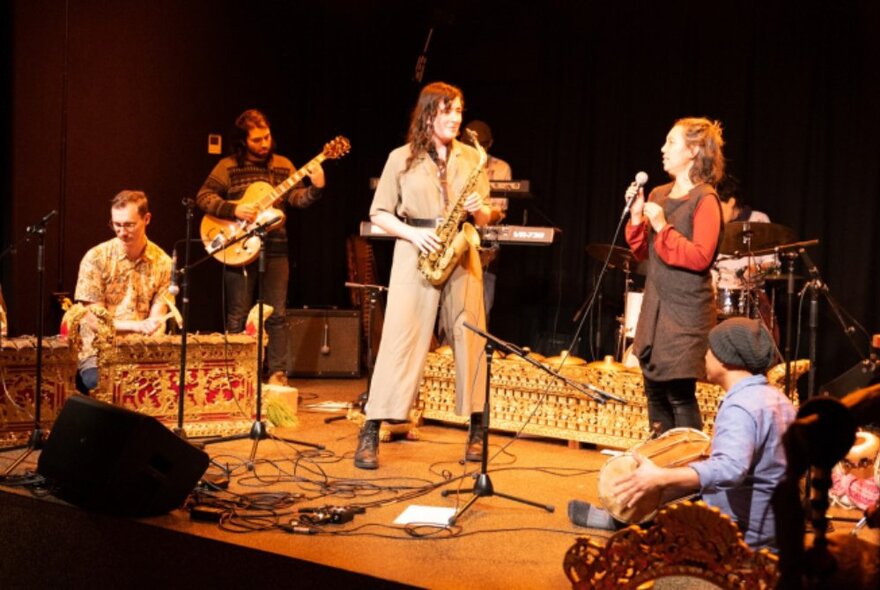 A band on stage with a saxophonist and woman holding a microphone up front. 