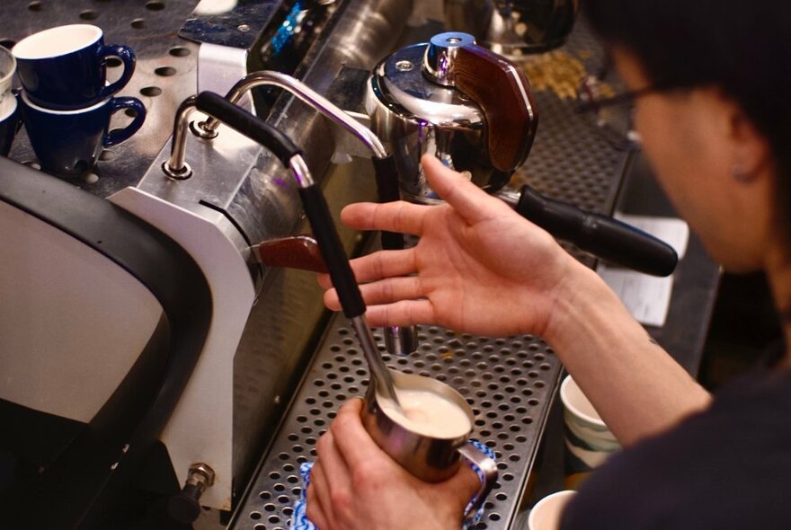 Looking down at a barista heating milk on an espresso machine. 