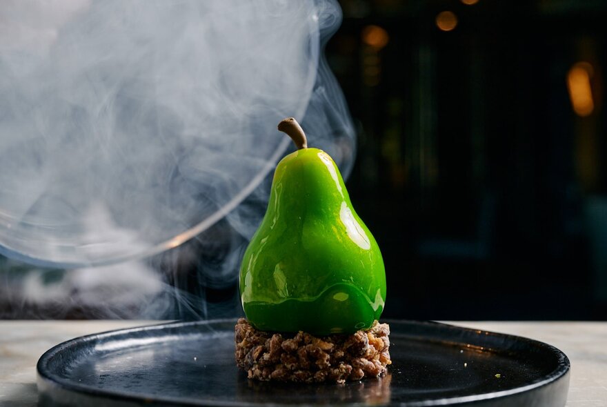 A stunning desert with a bright green pear atop a cake of nuts or seeds. 