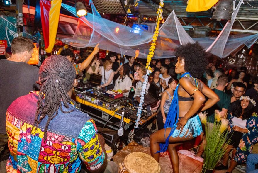 The Section 8 outdoor bar with people gathered socialising and dancing, while a solo dancer performs on a small stage in front of the DJ mixing desk.