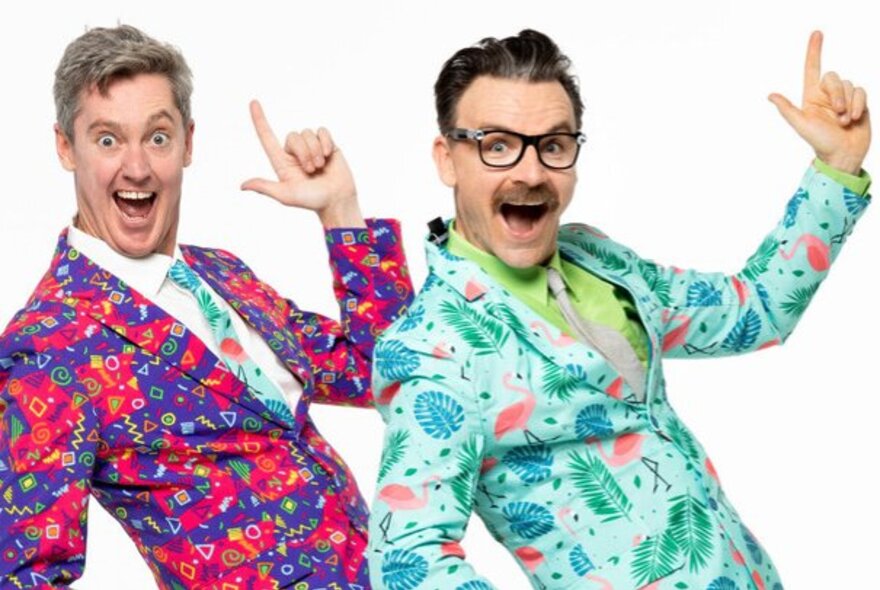 Two men in brightly patterned suits leaning back with one index finger in the air and mouths open in surprise. 