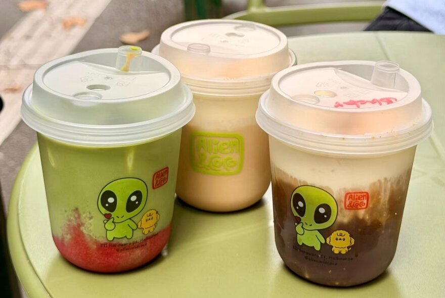 Cups of matcha and yuzu coffee in takeaway containers with alien graphics.