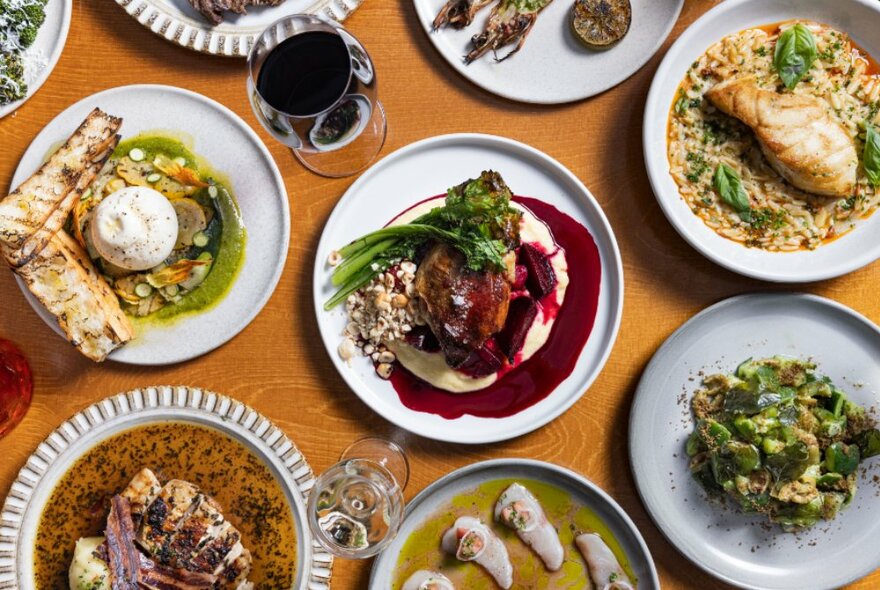 Looking down on a table with various plates of food and glasses of wine. 