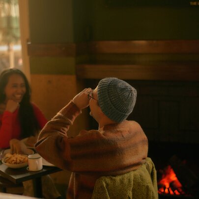 Two friends seated across from each other at an indoor table at The Lincoln, laughing and enjoying their meal in front of an open fire.