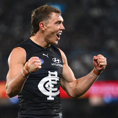 A Carlton AFL player celebrating on the field with his mouth open and his fists clenched.