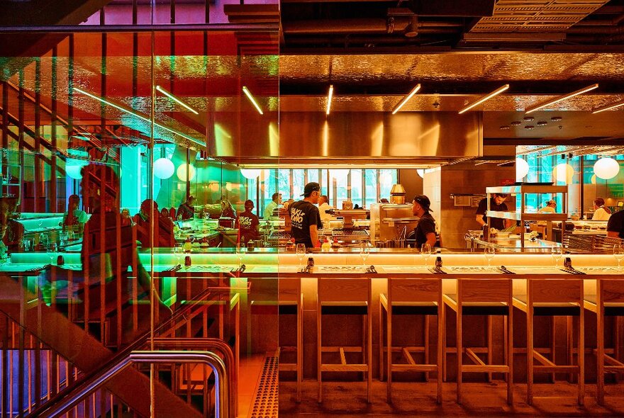 The warm timber and golden interior of Yakimono restaurant showing the open central kitchen and a row of high bar stools.