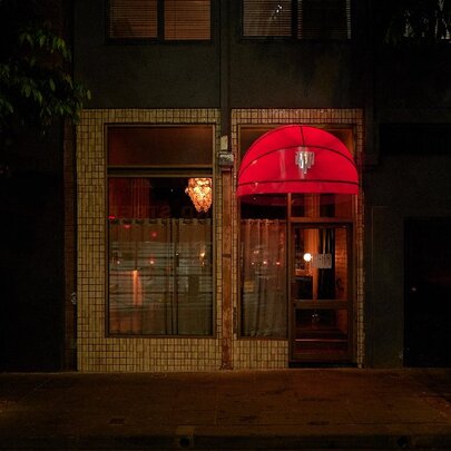 A glowing red street canopy over a dark doorway in a laneway.