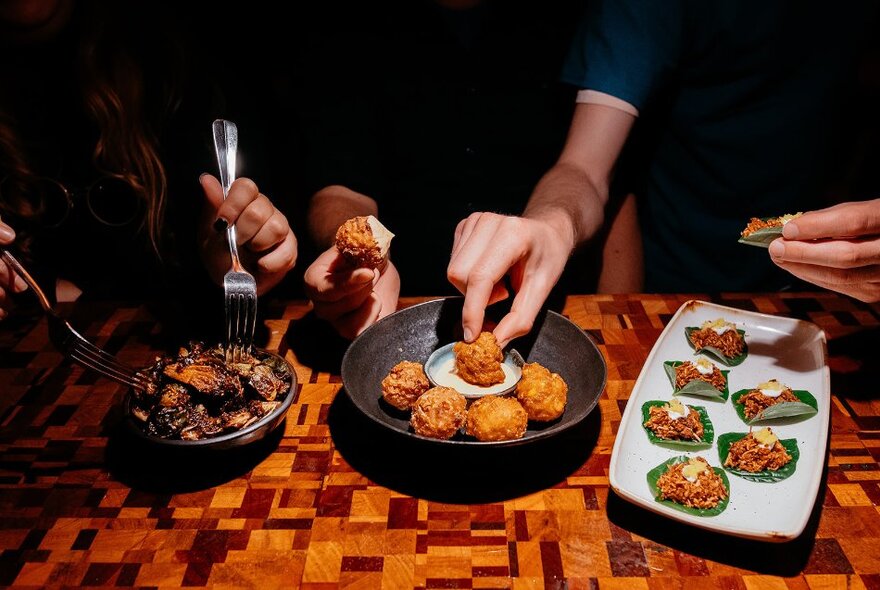 People sampling small bites of food from share plates on a table.