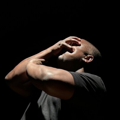 Actor with his hands over his face in a dark setting.