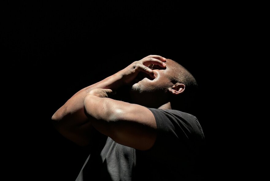 Actor with his hands over his face in a dark setting.