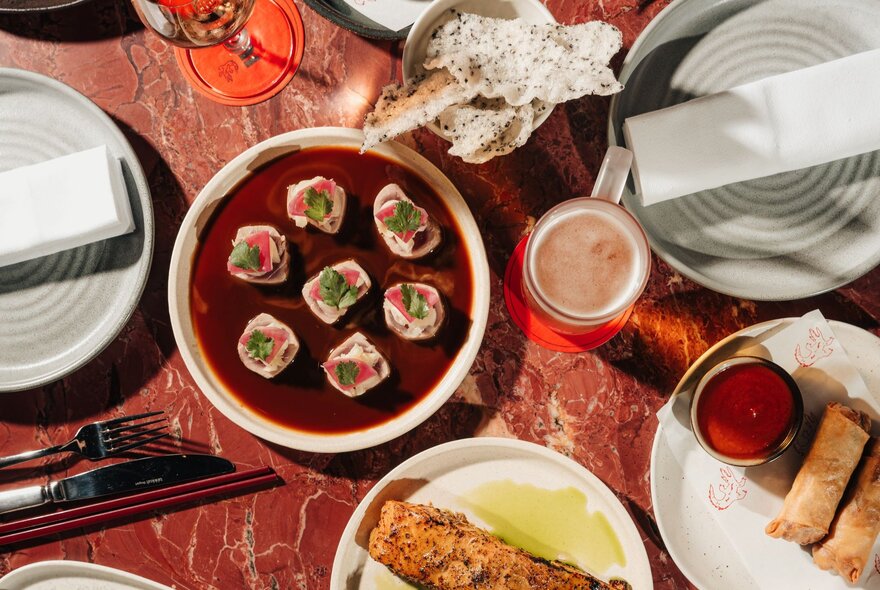 A selection of Asian food on a red marble table, seen from above.
