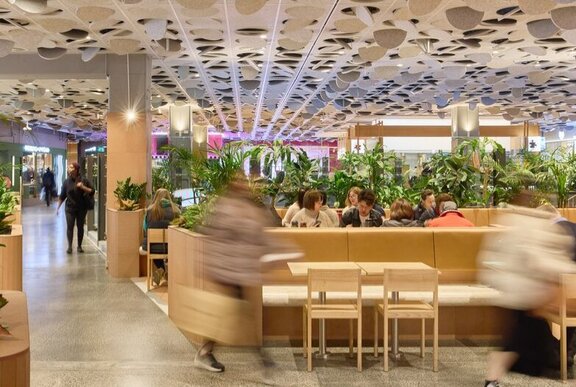 Food court with plants and wooden seating.