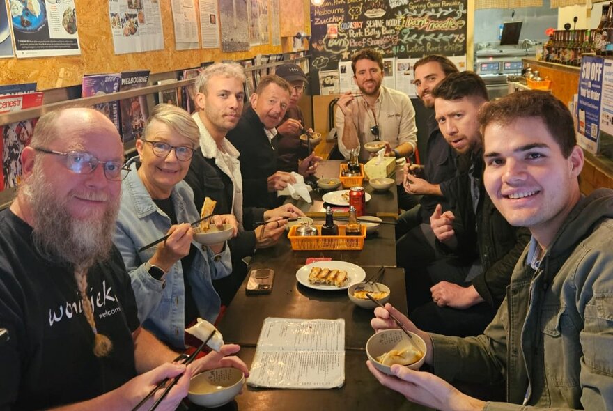 A group of people enjoying dumplings at a long table in a compact restaurant.