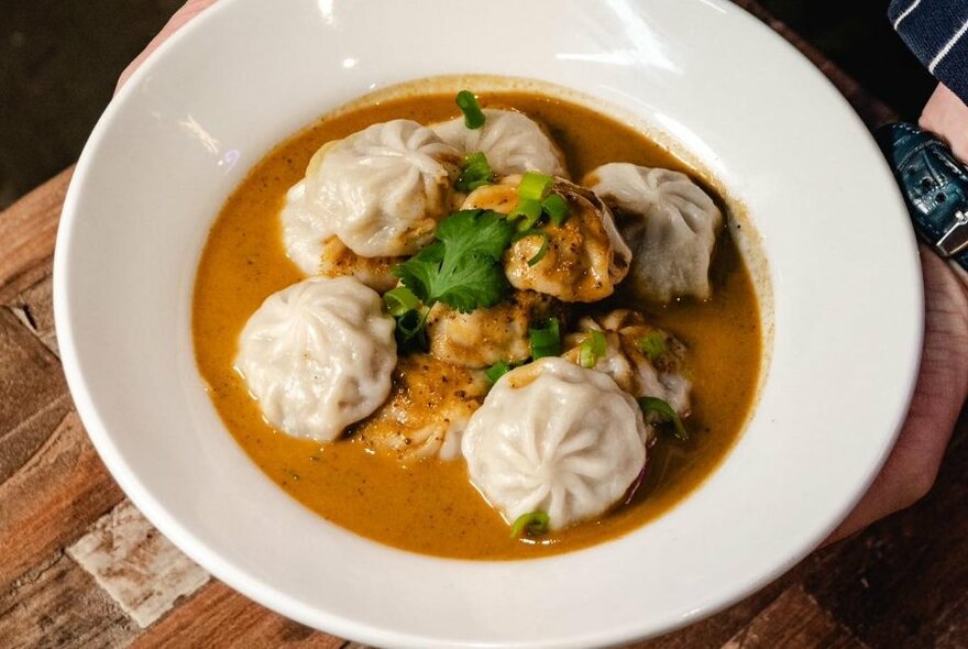 A low bowl filled with dumplings in a soupy broth.