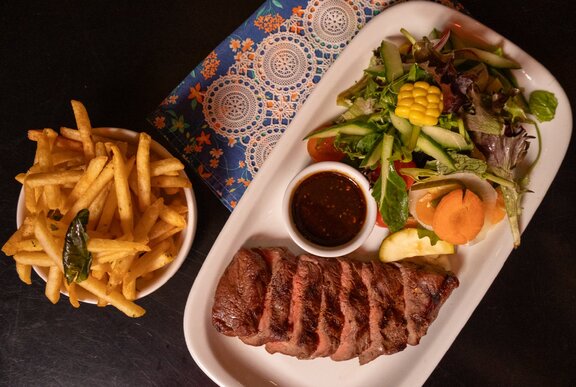 A sliced steak served with a side of fries, salad, and a dipping sauce. 