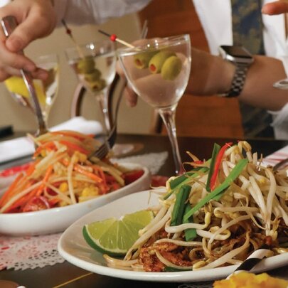 Hands using forks to select food from shared platters, with martini cocktails next to the plates.