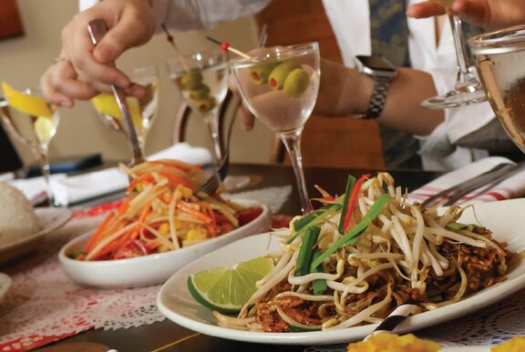 Hands using forks to select food from shared platters, with martini cocktails next to the plates.