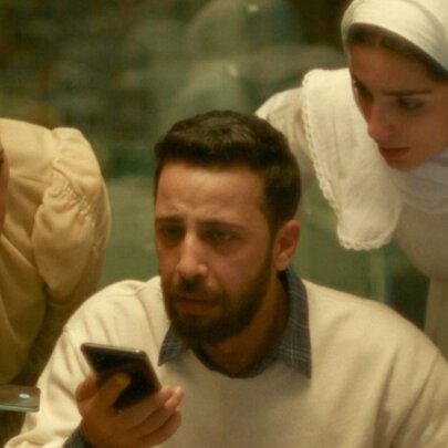 A man and two women speaking into a mobile phone, looking concerned.