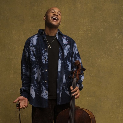Cellist Sheku Kanneh-Mason, tilting his head back and smiling, holding his cello in his hand.